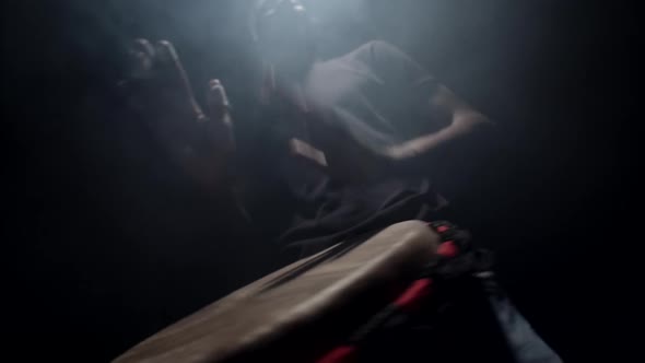 African American man plays an African folk musical instrument, bongo drum, in dark studio