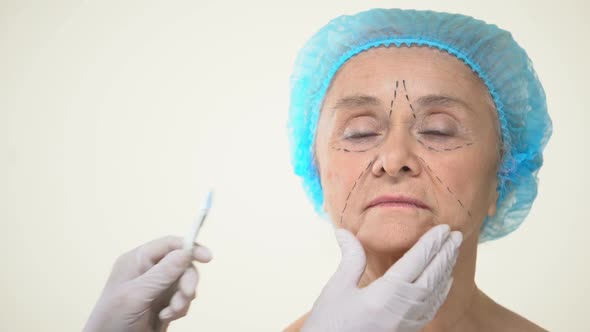 Surgeon Placing Scalpel to Aging Female Patient Face With Marks, Face Lifting