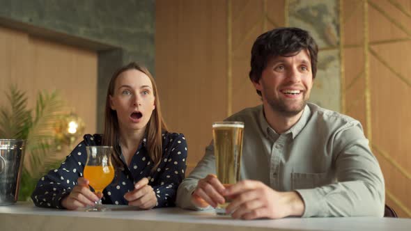 Young Couple is Rooting for Their Favorite Sports Team in a Bar Watching a Match Online