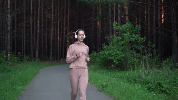 A Girl Jogs in the Park and Listens to Music on Headphones