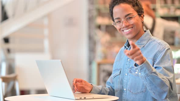 Cheerful African Woman with Laptop Pointing at the Camera 