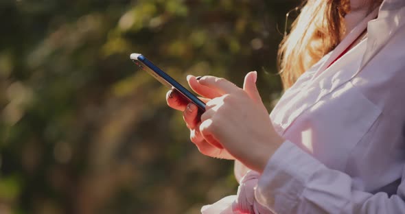 Hands of Young Woman Using Phone Sitting in the Park