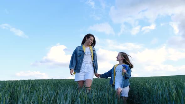 Mom and Daughter Walk in a Green Field of Young Wheat