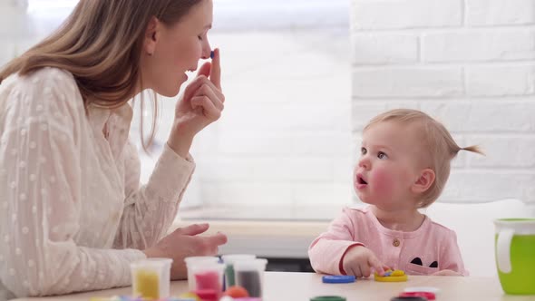 Mom and Little Daughter Sitting in Kitchen and Playing Multicolored Plasticine Mother and Daughter