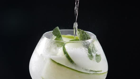 Bartender Making Refreshing Cocktail Lemonade with Ice, Cucumber, Lemon. Bubbles Running Up in Glass