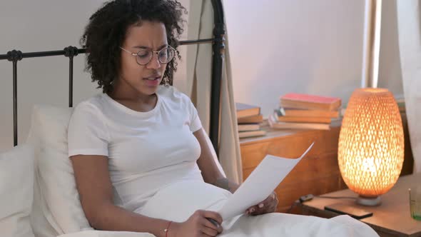 Young African Woman Reacting To Loss on Documents in Bed 