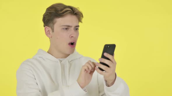 Young Man Loss on Smartphone on Yellow Background