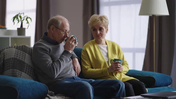 Old Man and Woman are Resting at Home at Weekend Retirees are Drinking Tea Sitting on Couch in