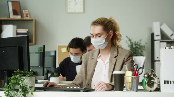 Young Blonde Woman Wearing Medical Protective Face Mask Working in Office Businesswoman Typing on