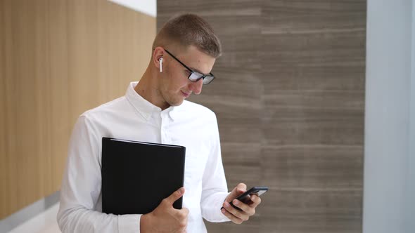 Businessman In Wireless Earphones Using Smartphone In Office Hall