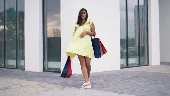 Beautiful Girl Model in a Long Dress After Shopping with Colored Bags in Hands