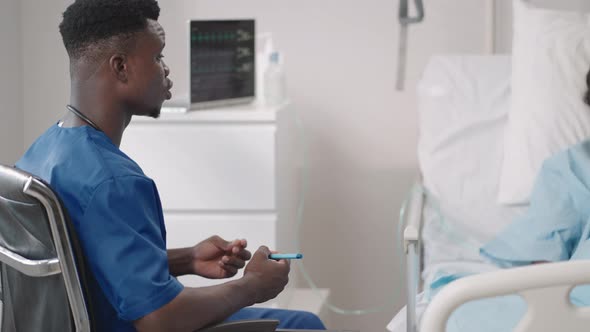 An African Male Doctor Interviews a Patient Lying in a Hospital Bed with an Oxygen Mask