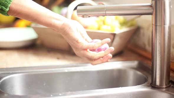 Woman washing plum at kitchen sink