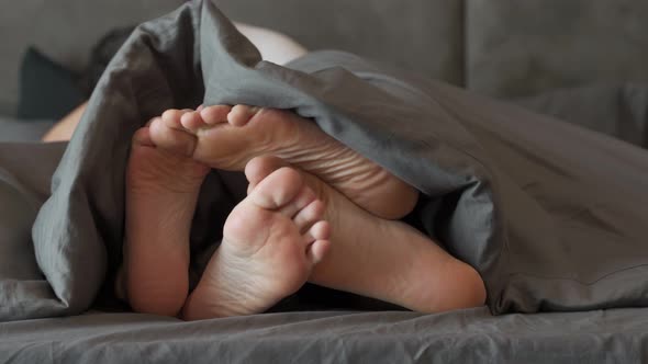 Feet of a Couple in Love on the Bed Having Sex Under the Blanket