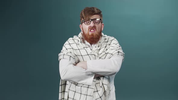 A Bearded Man in Eyeglasses Stands Crossing His Arms and Sneezes