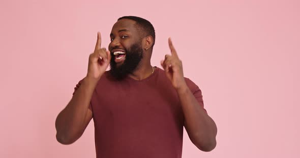 Young African American Man Points Up Dancing Isolated on Pink Background