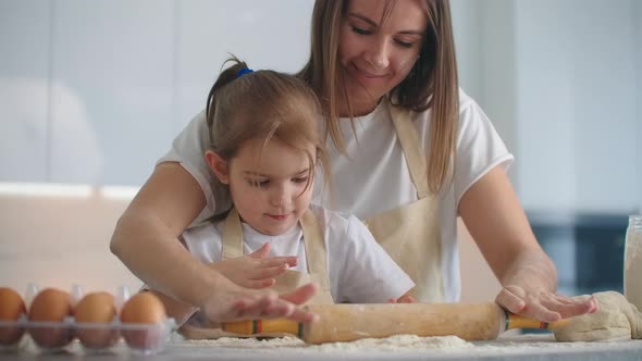 Daughter and Mother at Home in the Kitchen in Aprons Pour Flour Roll Out with a Rolling Pin and