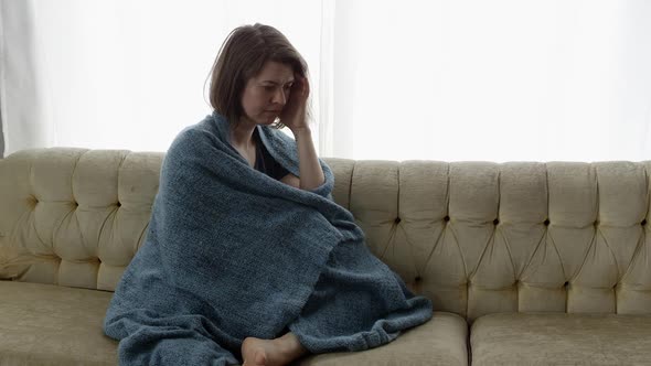 Sad woman sitting on couch wrapped in blanket