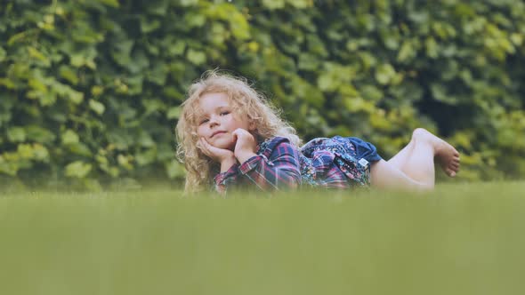 A Little Curlyhaired Girl Lies on the Grass in the Garden