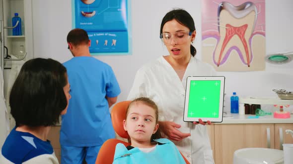 Stomatologist Woman Looking at Green Screen Tablet While Speaking with Mother