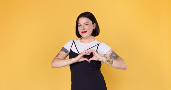 Young unusual woman with tattoos showing hands sign heart shape on chest