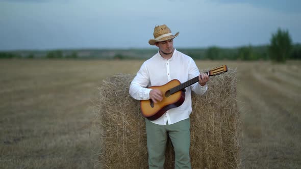 Man Wearing a Straw Hat Playing the Guitar About a Haystack