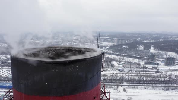 Aerial Survey Over the Tops of Two Smoking Factory Pipes and the Snow-capped City Lying Below. alt