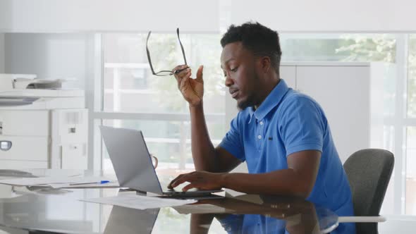 Tired Young Businessman Overworking Sitting at Desk with Laptop in Modern Office