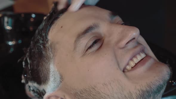 Young Man is Washed His Head in a Barber Shop He Smiles Closeup
