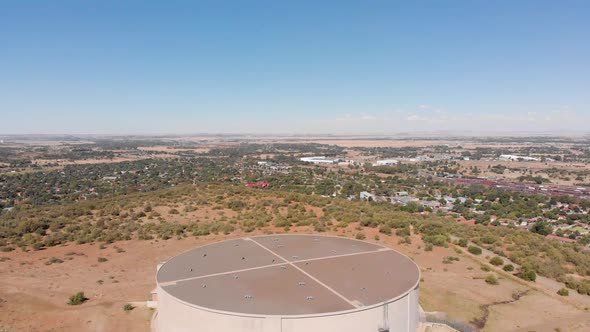 DRONE Reveal Shot of Water Supply Tank supplying water to a Town in the Background on a Sunny Day
