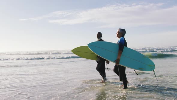 Senior african american couple walking with surfboards at the beach