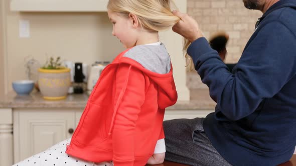 Father combing his daughter hair in the kitchen