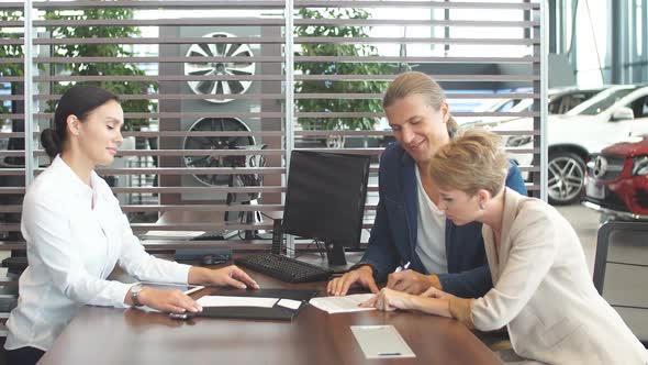 Beautiful Young Couple Signs Documents at Dealership Showroom