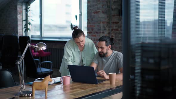 Two Coworkers are Discussing a Project While Sitting in Front of Their Laptops