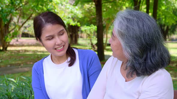 Happy senior mother with gray hair talk and laugh with daughter or caregiver in the park. Concept of