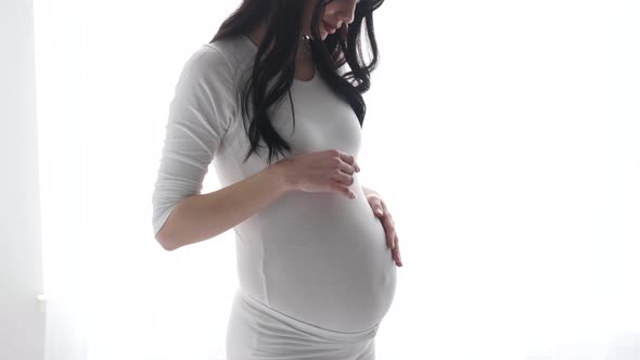 Pregnant Woman Touching Baby Belly In White Interior