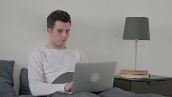 Man Working on Laptop in Bed
