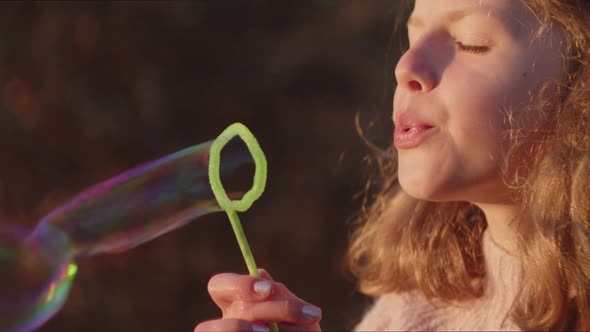 Girl Blowing Bubbles From Wand In Sunlight
