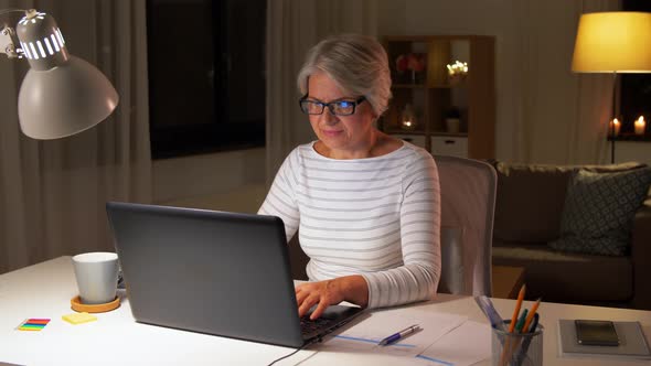 Happy Senior Woman with Laptop at Home in Evening