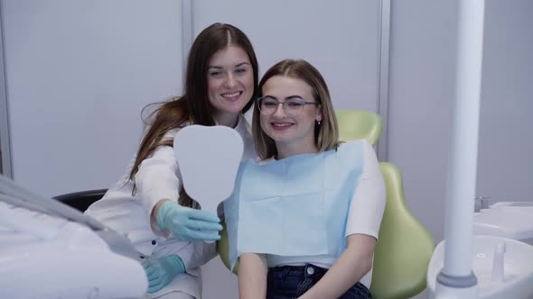 Happy Dentist Looking and Smiling with Her Patient at Dental Mirror