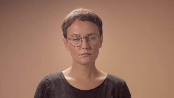 Caucasian Woman with Short Haircut Wears Glasses in Studio on Beige Background