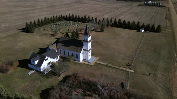 Drone orbiting around beautiful old country church in Canadian prairie. Young man standing in front