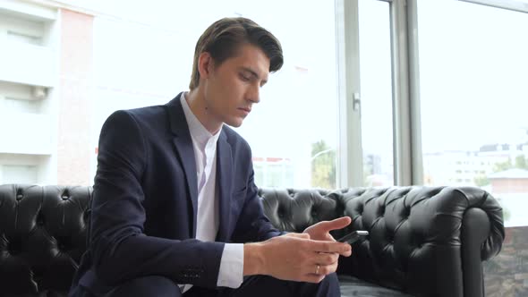 Male millennial professional holding modern smartphone texting message in office