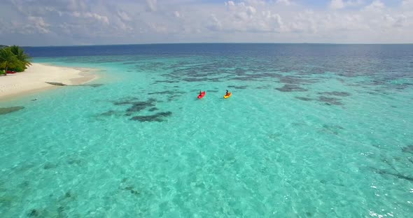 Aerial drone view of a man and woman couple kayaking around a tropical island.