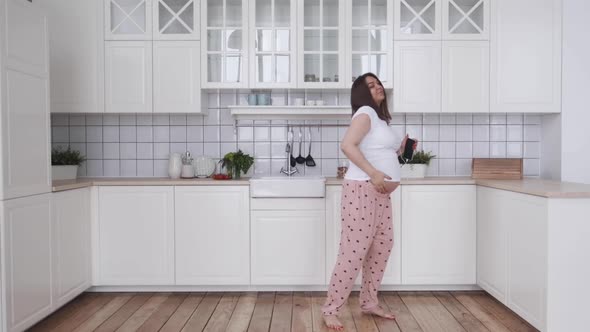 Happy Cozy Dancing Pregnant Woman in a White Kitchen