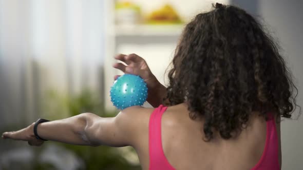 Fit young lady rolling massaging ball over arm, view from behind, relaxation