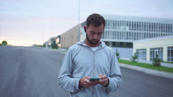 Male Jogger Holding Phone in Hand Before Running. Sport Man Checking Results on Smartphone Outdoor