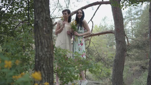 Portrait Two Beautiful Women in Short Dresses Standing on Rocky Ground with Wild Flowers and Looking