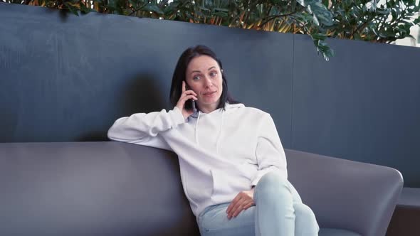 Smiling Young Business Woman of European Appearance in a White Sweater Sits in a Cozy Green Place in