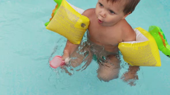 Kid in Oversleeves Swims in the Pool in the Yard